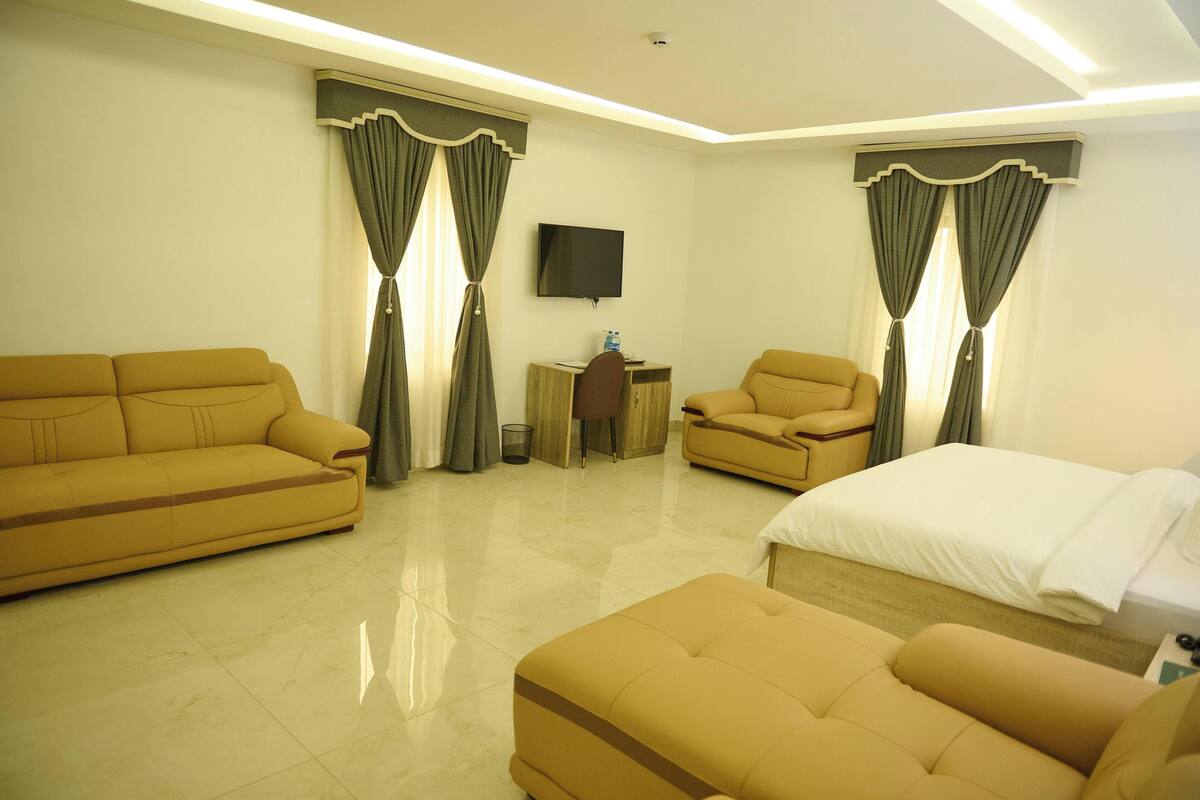 A hotel room with a sofa, a chair, a bed, a TV, and a small table.