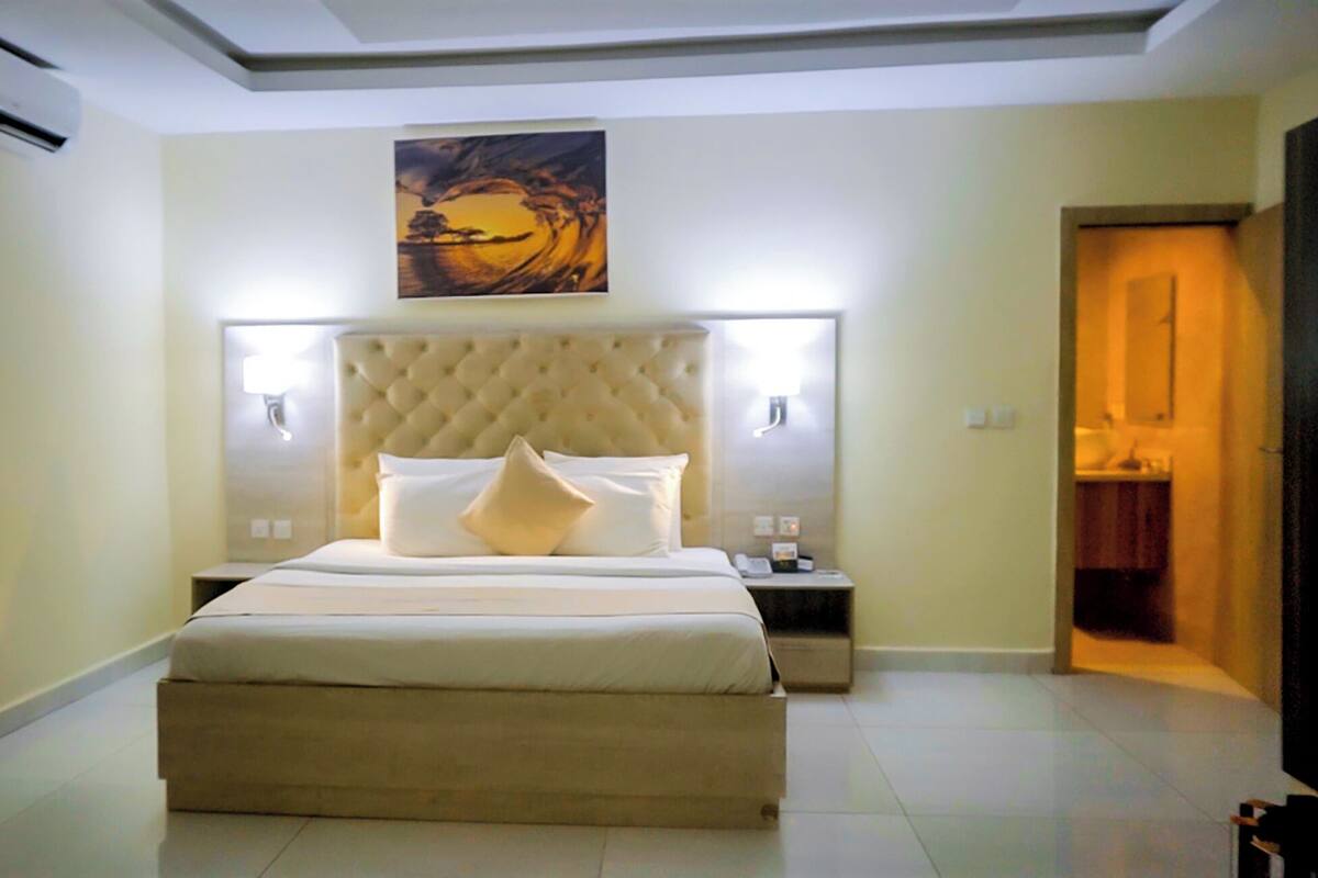 A hotel room with a large bed, a tufted headboard, bedside lamps, and a painting above the bed.