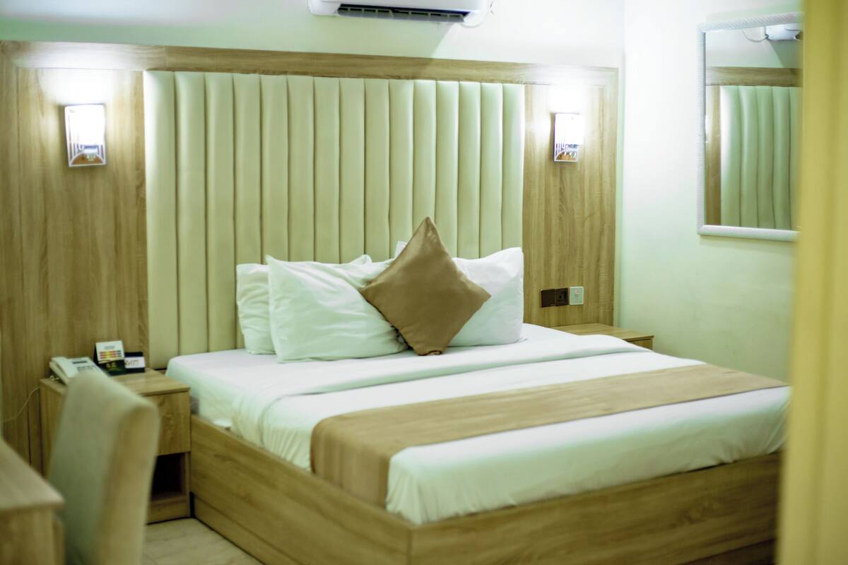 A neatly made bed with white and brown bedding, a wooden headboard, and a bedside table with a phone and a small item on it.