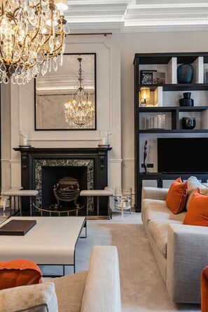 A living room with a fireplace, a chandelier, a bookshelf, and a sofa. - Cadogan Square Ultra-luxe 4BR Private Garden (London)