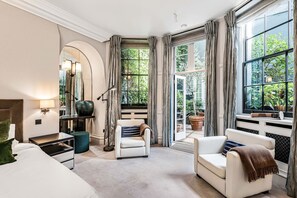 A modern hotel room with a large window, a sofa, a chair, a desk, and a mirror. - Cadogan Square Ultra-luxe 4BR Private Garden (London)