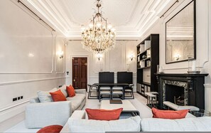 A spacious living room with a chandelier, a fireplace, and a dining area with a table and chairs. - Cadogan Square Ultra-luxe 4BR Private Garden (London)