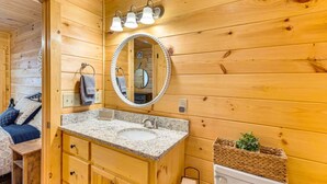 Baño de cabaña de madera con lavamanos de encimera de granito, un espejo redondo y armarios de madera.