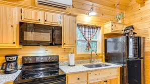Una cocina compacta con armarios de madera, un refrigerador de acero inoxidable, un microondas, una estufa y una cafetera.