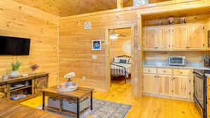 Interior de una cabaña de madera con sala de estar, cocina y dormitorio.