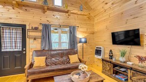 Interior acogedor de una cabaña de madera con un sofá de cuero, un televisor de pantalla plana y una mesa de centro de madera rústica.