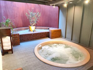 Ein Wellnessbereich mit Whirlpool, einer Holzbank, einem Topfpflanzen und einer Backsteinwand.