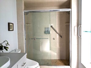 Un baño con ducha envuelta en vidrio, inodoro y lavamanos.
