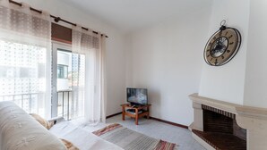 Una sala de estar con sofá, televisor sobre un mueble, chimenea y un ventanal con cortinas.