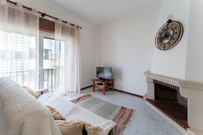 A living room with a sofa, a television on a stand, a fireplace, and a large window with curtains. - Wild Atlantic 2 bedroom apartment (Aguieira)