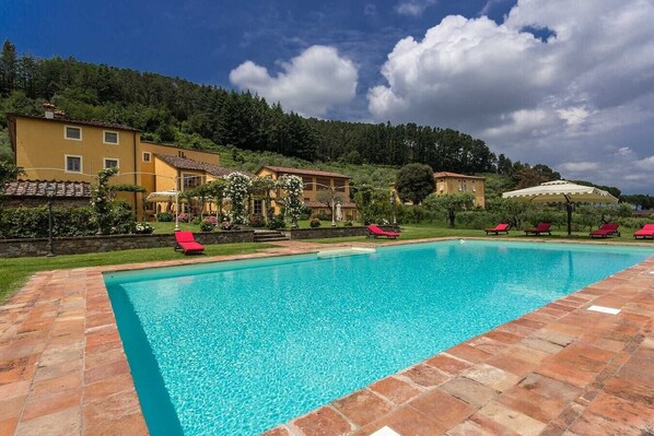 Una piscina con sillas de descanso rojas, rodeada de baldosas de terracota y un paisaje con colinas.