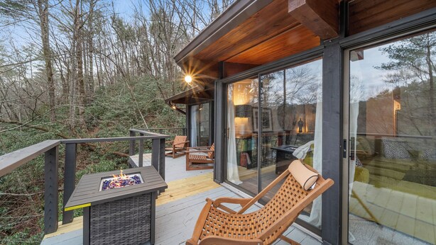 Eine moderne Terrassenanlage im Freien mit einer verglasten Fläche, Holzmöbeln und einem Feuerbereich.
