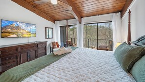 Ein Schlafzimmer mit einem großen Bett, Holzboden, einem Flachbildfernseher, einem Schminktisch und Blick ins Freie.