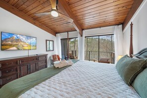 Ein Schlafzimmer mit einem großen Bett, Holzboden, einem Flachbildfernseher, einem Schminktisch und Blick ins Freie.