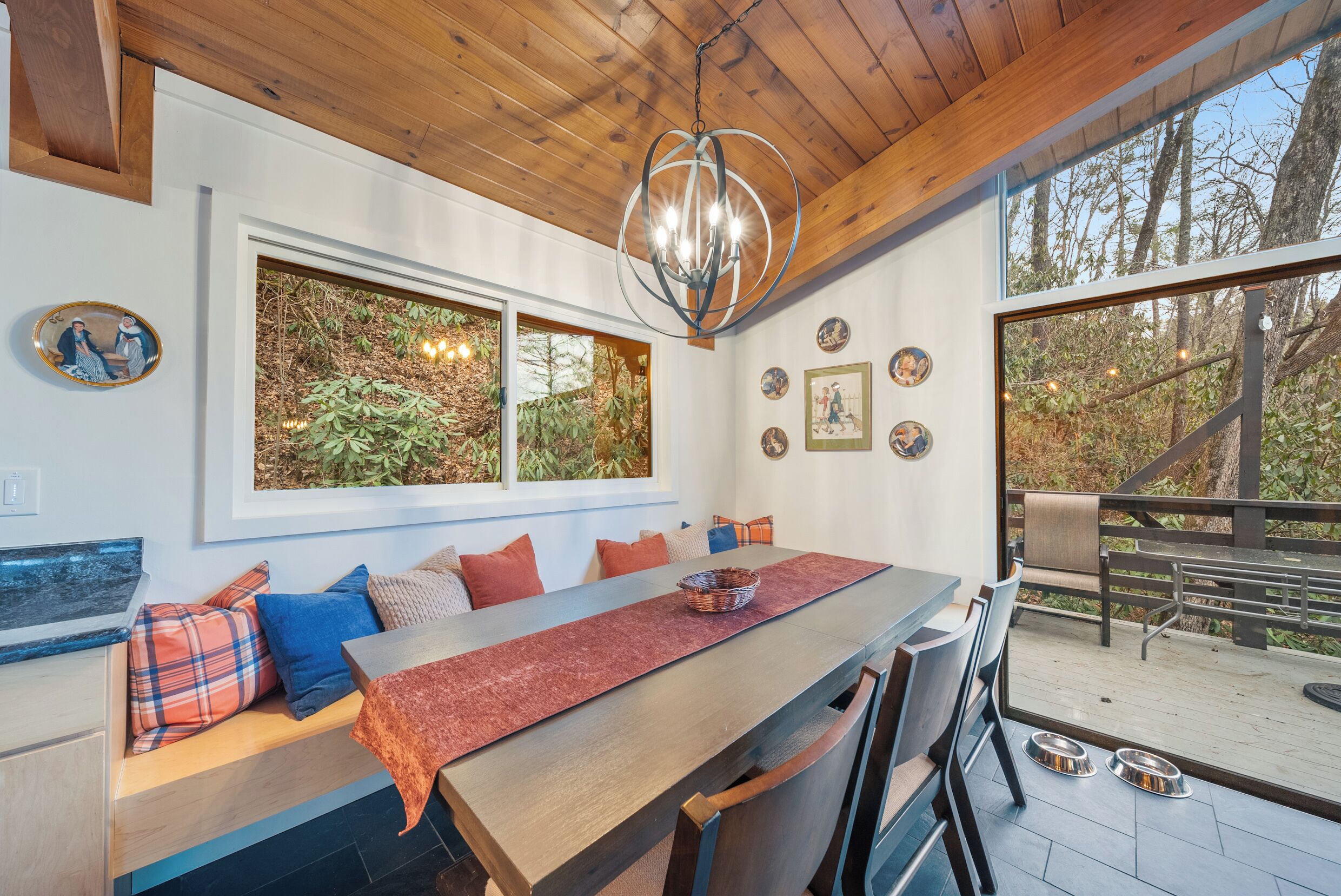 Un espace repas moderne avec une table en bois, des bancs et une grande fenêtre donnant sur une forêt.