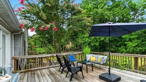 Eine Holzterrasse mit Gartenmöbeln, darunter Stühle und ein Tisch, sowie ein großer Sonnenschirm.