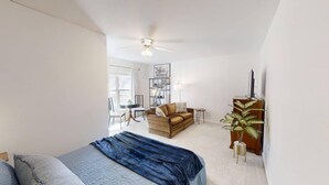 Ein Schlafzimmer mit Bett, einer Couch, einem Fernseher, einer Pflanze und einem Deckenventilator.
