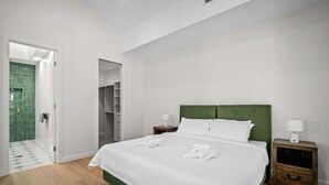 Camera d'albergo con un letto grande, una testiera verde, biancheria da letto bianca, un comodino in legno e una cabina armadio.