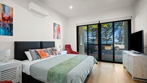 A modern hotel room with a large bed, a red chair, a TV, and a view of the outside.