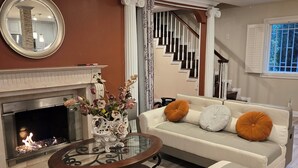 Ein Wohnzimmer mit Kamin, einer Couch mit Kissen, einem Couchtisch und einer Treppe.