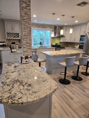 A modern kitchen with marble countertops, white cabinetry, and a central island with bar stools. - Home with breathtaking views (Monterey Park)