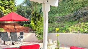 Eine Terrassenfläche mit Tischplatte aus Glas, roten Kissen und Gartenmöbeln.