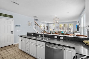 A modern kitchen with a granite countertop, white cabinets, and a stainless steel sink. - Beach house in Heart of Surfside Beach, SC (Surfside Beach)