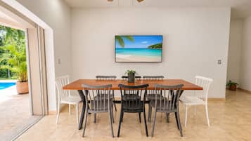 Un comedor con una mesa y sillas de madera, un cuadro de una playa y vistas a una piscina.