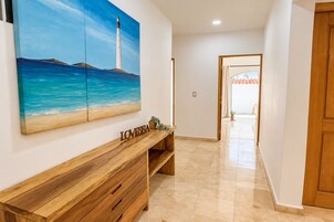 Un pasillo con un banco de madera, un cuadro de un faro y una puerta que da a otra habitación.