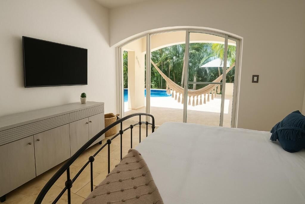 Une chambre avec un lit, une télévision, un canapé et une vue sur une piscine et des palmiers, visible à travers une porte vitrée.