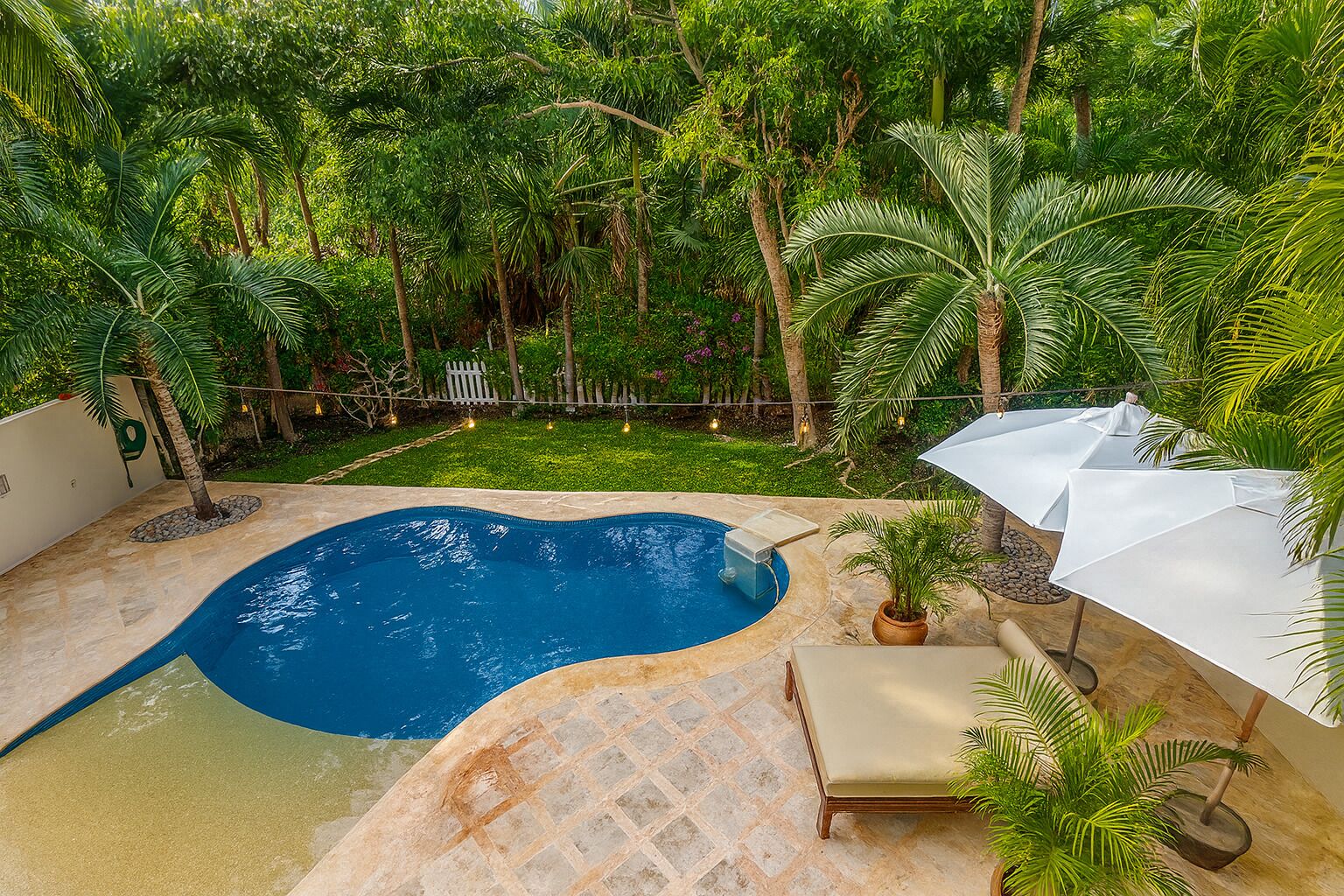 A swimming pool surrounded by lush greenery, a lounge area with a chair, and a white umbrella.