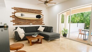 Un salon moderne avec un canapé d’angle, une table basse en bois et une décoration murale représentant une planche de surf.