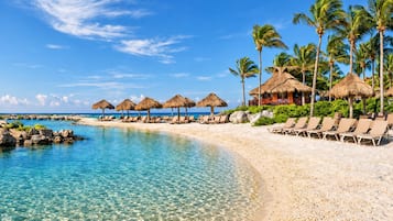 Un complexe hôtelier de bord de mer avec une eau turquoise cristalline, des chaises longues et des parasols en chaume.