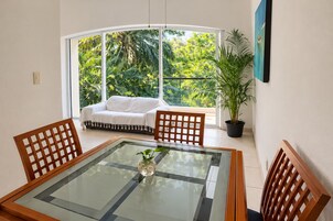 Una habitación con una mesa de vidrio, sillas de madera, un sofá y una planta en maceta.