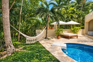 A poolside area with a hammock, lounge chairs, and a small garden. - Pool Jacuzzi Private Villa 7BR (Puerto Aventuras)
