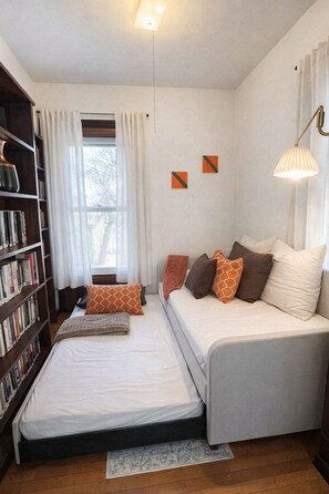 Un dormitorio acogedor con dos camas, una estantería y una ventana con cortinas.