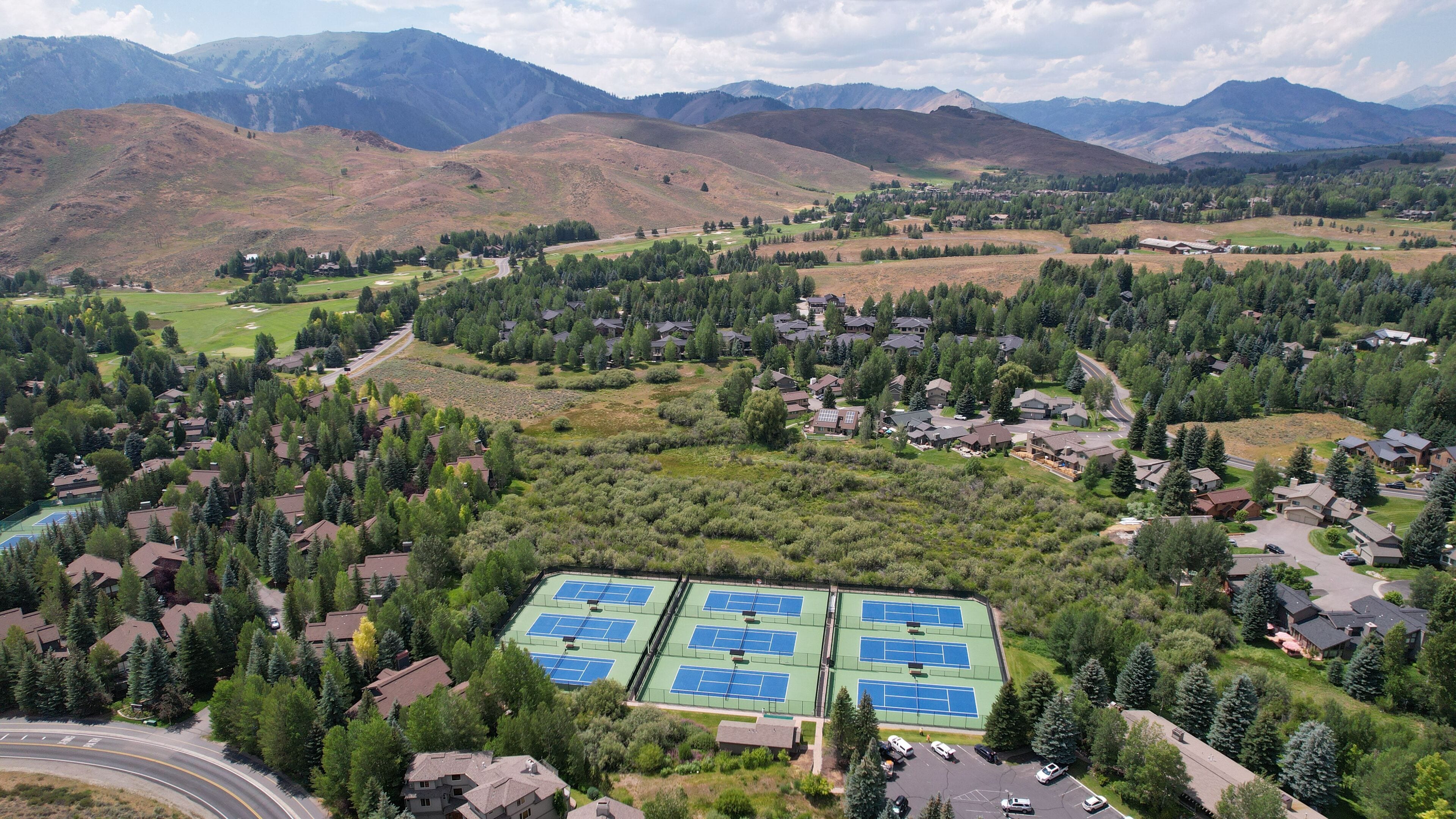 Vue aérienne d’un quartier résidentiel avec des maisons, un complexe de courts de tennis et les montagnes environnantes.