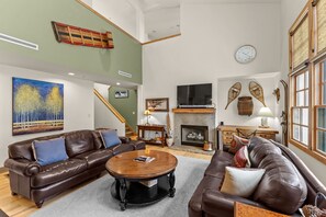 Ein geräumiges Wohnzimmer mit Ledersofas, einem Holztisch, einem Kamin und einem großen Gemälde.