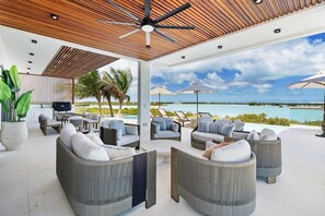 Een overdekt terras met banken en parasols, met uitzicht op een zwembad en de oceaan.