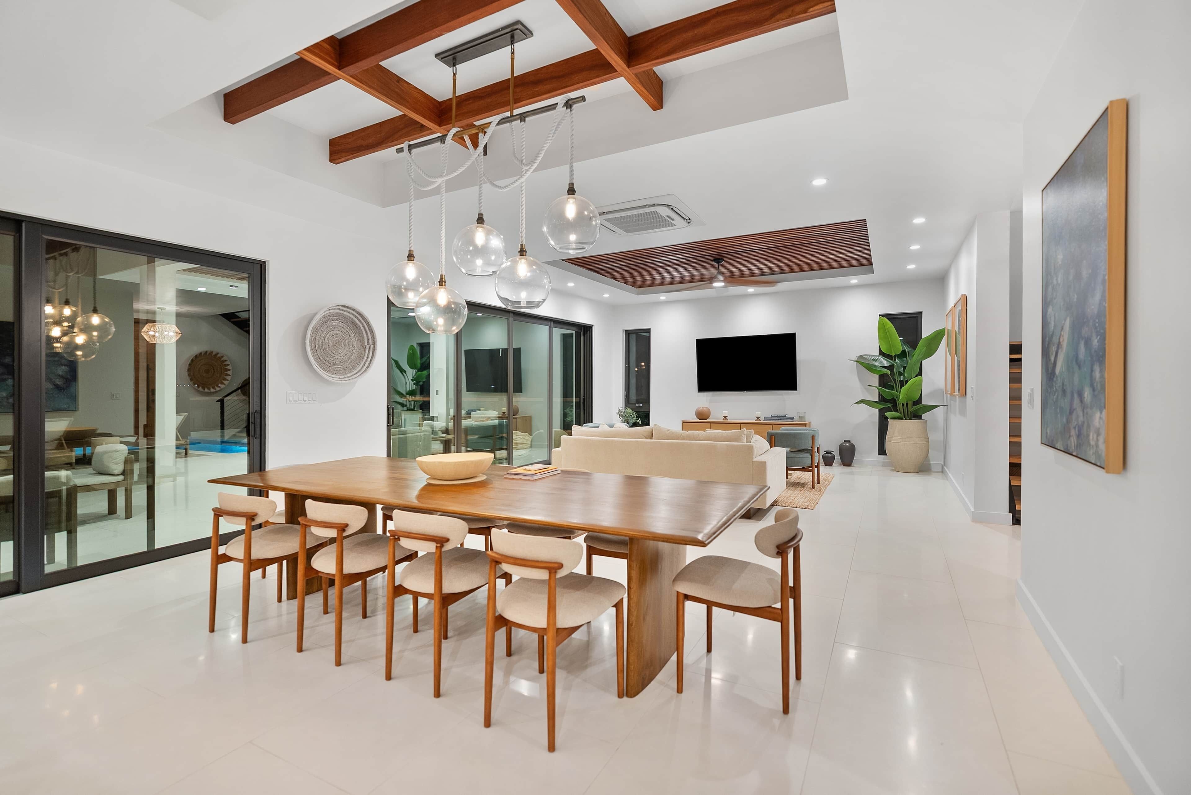 Un comedor moderno con una mesa y sillas de madera, lámparas colgantes y una planta grande.