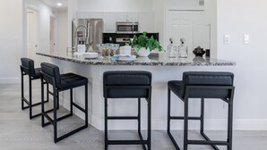 Een moderne keuken met een centraal eiland, barstoelen, roestvrijstalen apparatuur en een klok aan de muur.