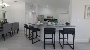Een moderne keuken met een centraal eiland, barstoelen en een eethoek met stoelen.
