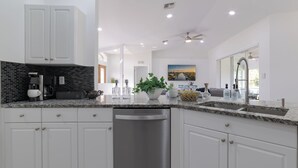 Een moderne keuken met witte kastjes, een RVS vaatwasser, een granieten aanrechtblad en een zwart achterspatbord.