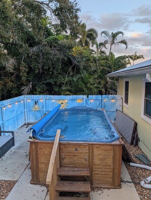 A wooden hot tub with a wooden ladder, surrounded by a blue fence, in a backyard with trees and a house. - Coastal Canopy, Private Pool: 15 Min to Beach (Bradenton)
