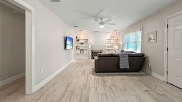 A spacious living area with a ceiling fan, a television mounted on the wall, a sofa, and a bookshelf.