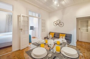 Ein Essbereich mit einem Tisch für vier Personen, einer Couch mit Kissen und einem an der Wand befestigten Fahrrad.