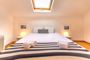 Ein Schlafzimmer mit Dachfenster, einem Bett mit gestreifter Bettwäsche, zwei Nachttischlampen und einer Heizung.