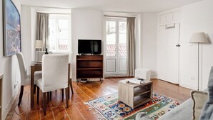 Ein Wohnzimmer mit Fernseher, weißen Sesseln, einem Holztisch und einem gemusterten Teppich.
