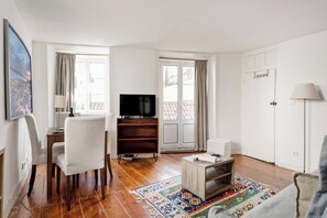 A living room with a TV, white chairs, a wooden coffee table, and a patterned rug. - Lisbon Cozy Nest in Santa Catarina (Lisbon)