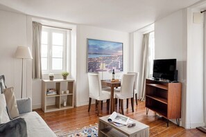 A modern living room with a dining area, a flat-screen TV, and a large window with a cityscape view. - Lisbon Cozy Nest in Santa Catarina (Lisbon)